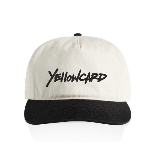 The Logo - White Snapback (Pre-Order) is a white cap with a black brim featuring bold, stylized "Yellowcard" lettering on the front. This presale item includes a shipping notice before its expected 2026 release.